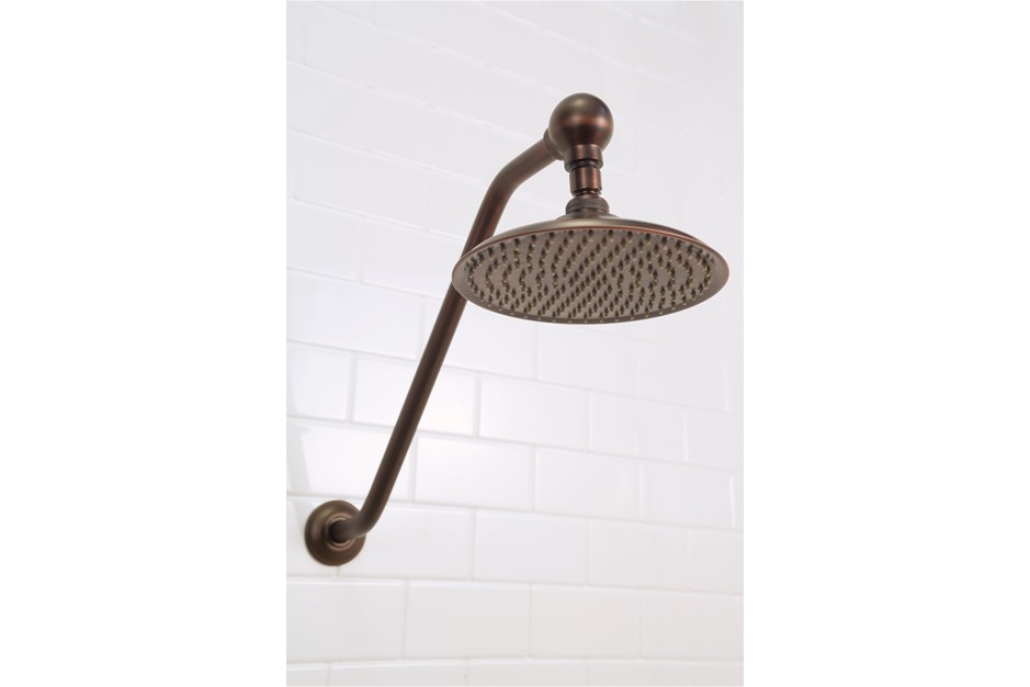 Close-up view of a bronze-finished rainfall shower head and curved arm mounted on a white tiled wall.