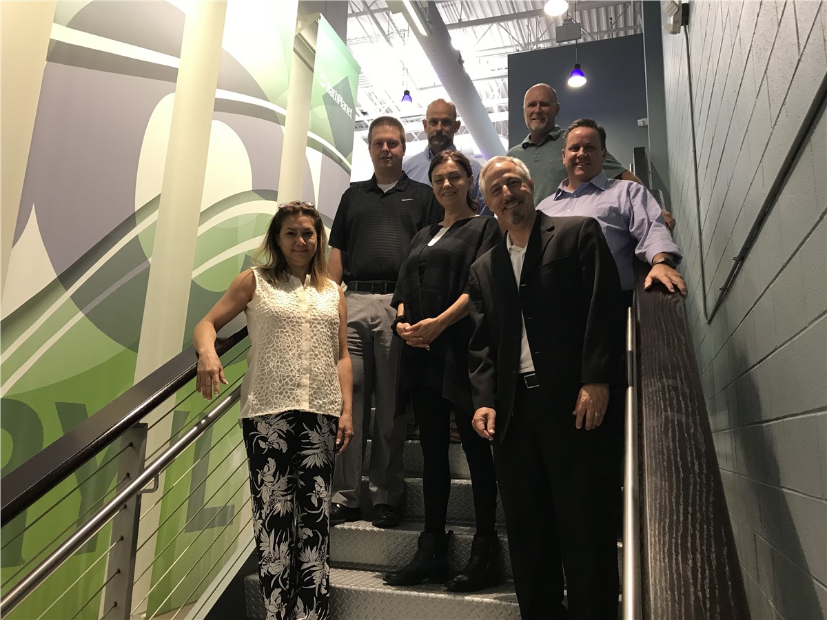 Group of seven smiling people of diverse age and ethnicity posing on a staircase, with a modern graphic mural behind them.