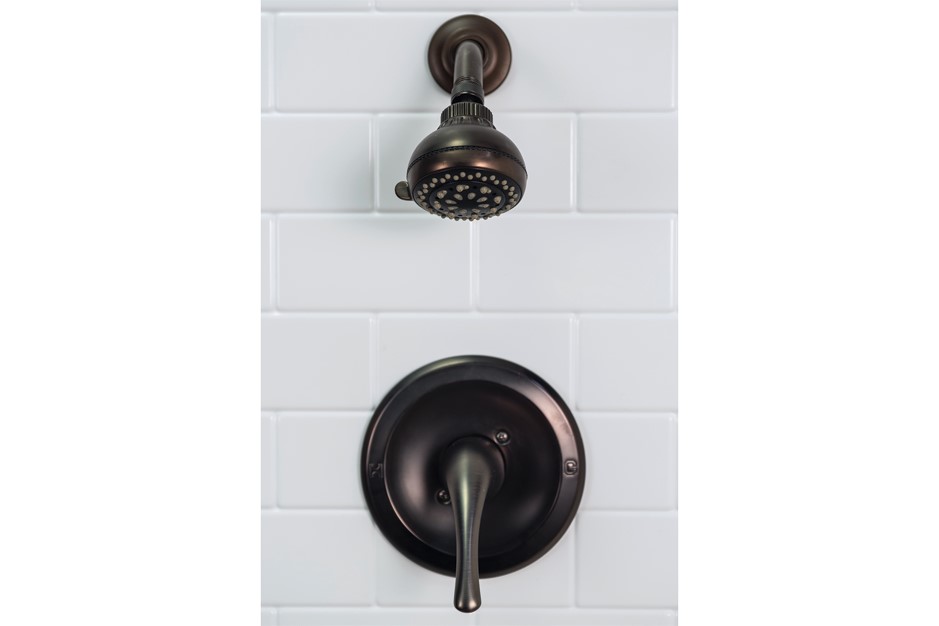 Close-up of a bronze shower head and faucet against a white tile wall.