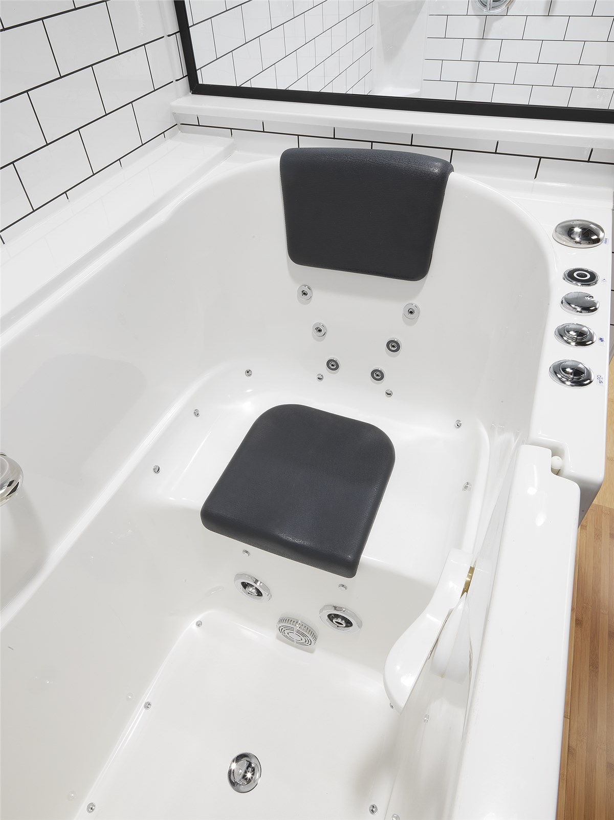 Close-up of a pristine, white walk-in bathtub featuring a gray seat and headrest, numerous whirlpool jets, a side-mounted control panel, and white subway tile on the adjacent wall.
