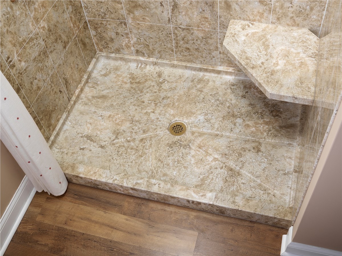 A walk-in shower with tan marble-patterned tiles on the walls and floor, featuring a built-in corner shower seat and a central drain. The shower borders a wood-patterned bathroom floor.