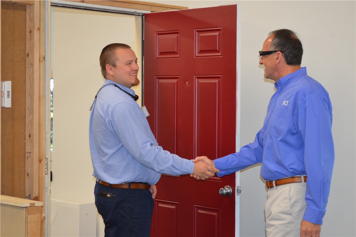 Two men in button-down shirts shaking hands in front of a red door.