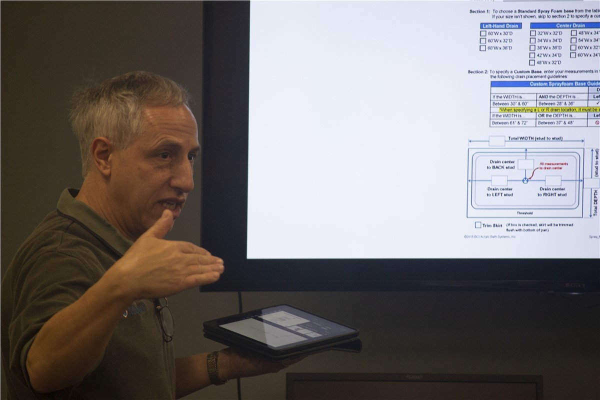 Man gesturing at screen showing custom spray foam base guide, holding a tablet.