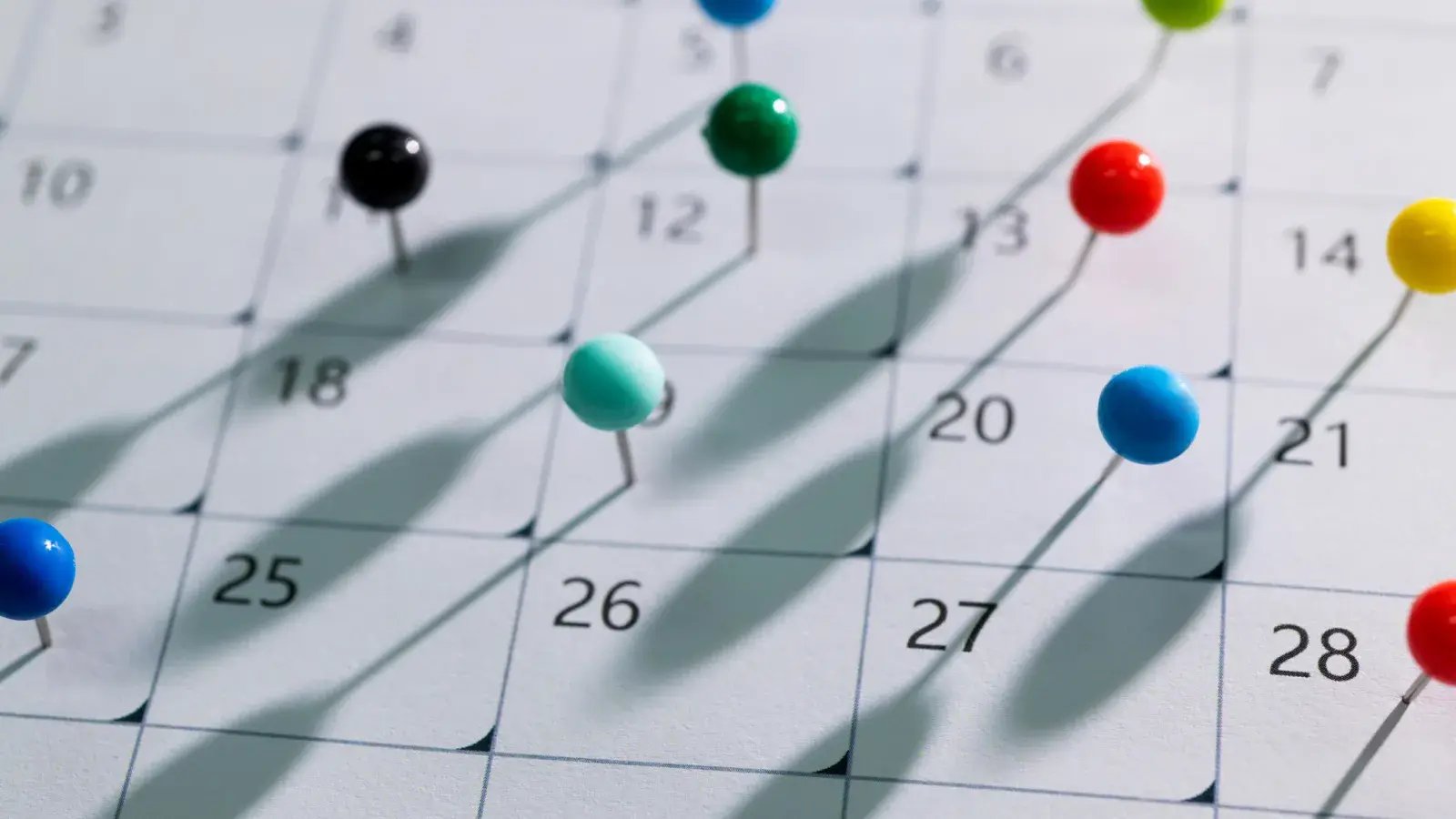 Close-up of a calendar grid marked with colorful push pins.