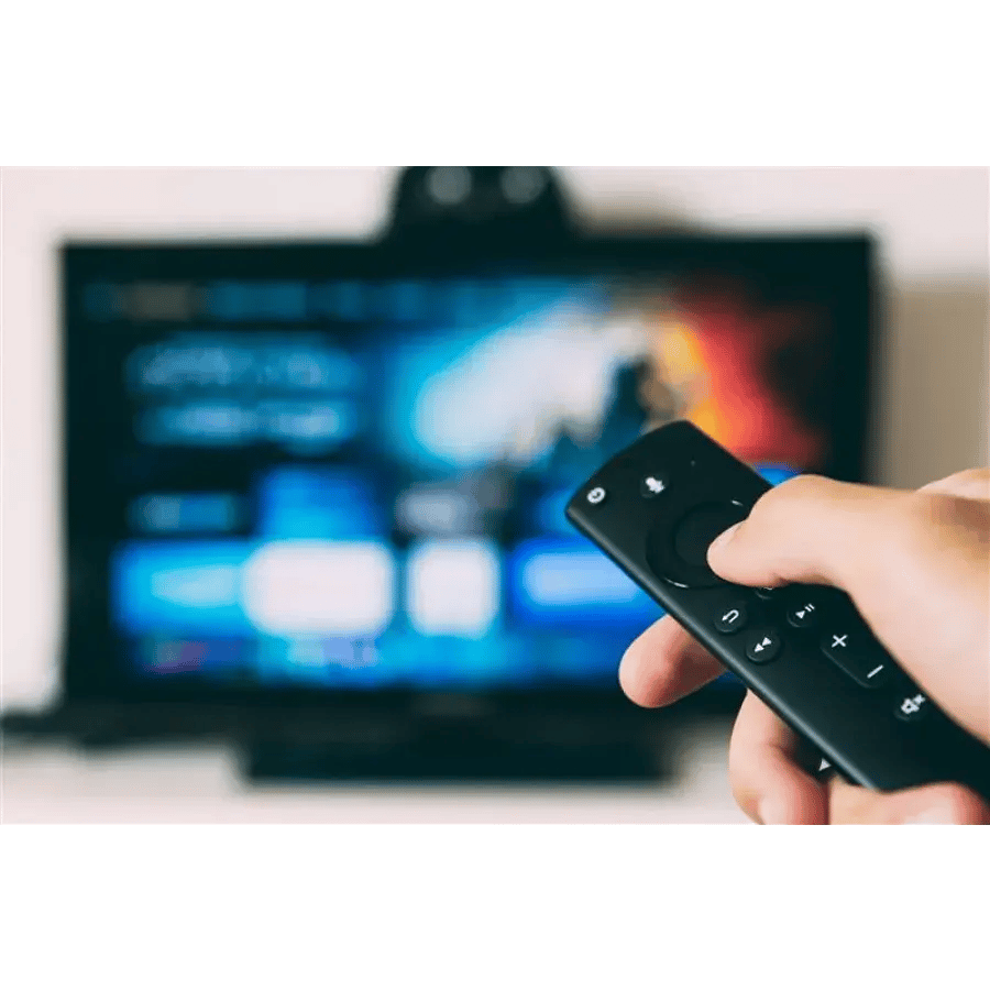Hand holding black remote control in front of a television displaying blurred colors.