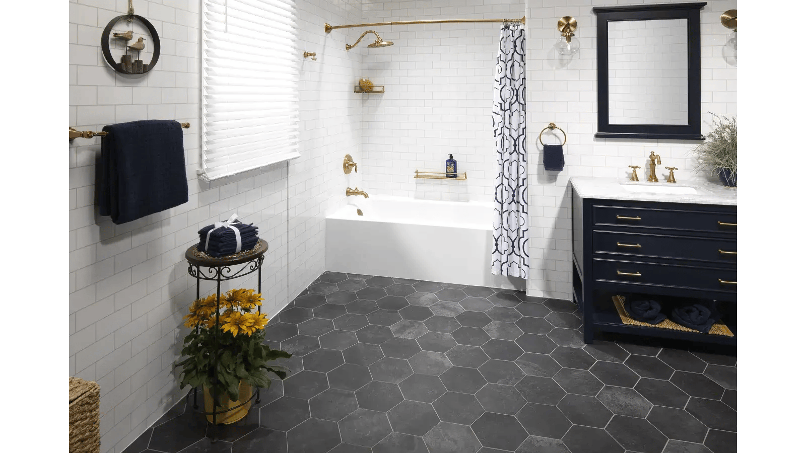 Bathroom interior with white subway tile walls, dark gray hexagonal floor tiles, navy blue vanity with gold fixtures, and a white bathtub with a navy blue patterned shower curtain.