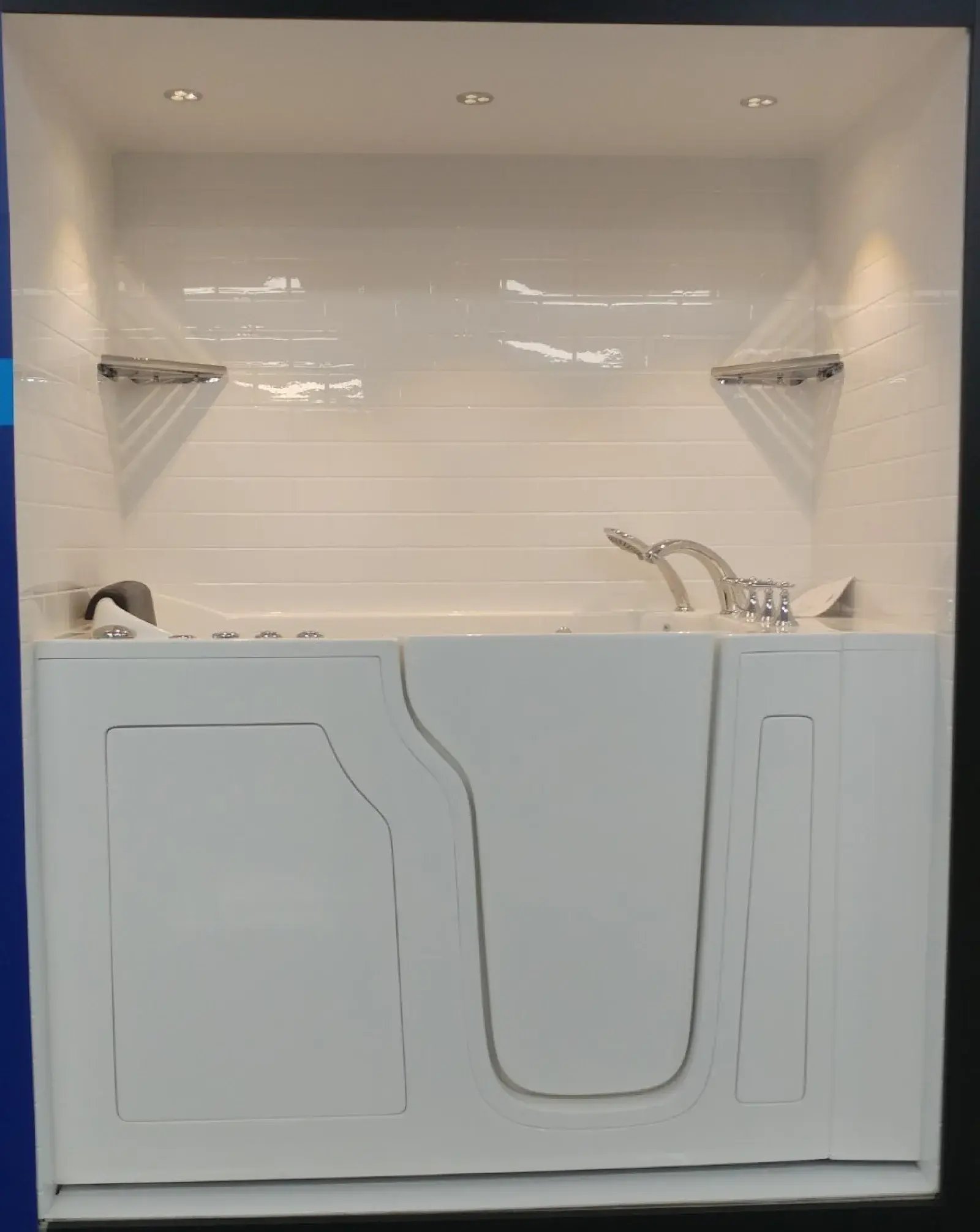 White accessible walk-in bathtub with silver faucet against a tiled wall.