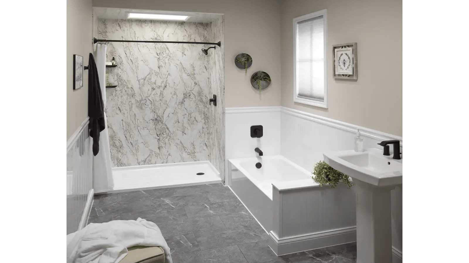 Modern bathroom with a white tub-shower combination against marble-patterned acrylic panels, a matching pedestal sink with matte black fixtures, gray tile flooring, and neutral-toned walls with white wainscoting.