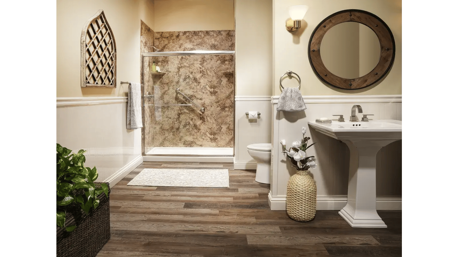 Bathroom featuring a pedestal sink, circular wooden-framed mirror, and a shower with marble wall panels and glass doors. Wooden floors and decorative wall panels contribute to a rustic aesthetic.