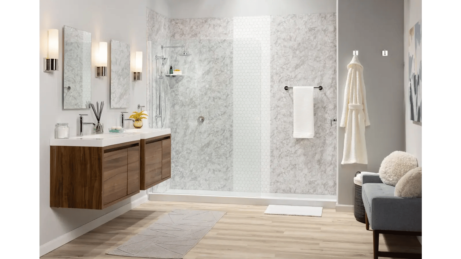 Brightly lit bathroom featuring a new shower design, double vanity, a gray, geometric patterned rug, and a blue upholstered bench.