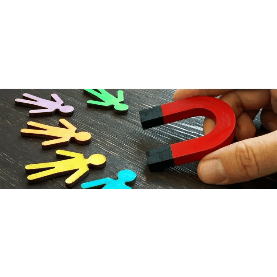 Hand holding a red horseshoe magnet over wooden table with scattered, multicolored figure-shaped tokens.