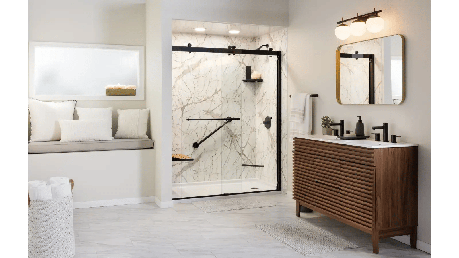 Bathroom interior featuring a shower with white marbled walls and black trim, a sliding glass door, matte black fixtures, a wooden bench with wooden slats, and handrails. There is a vanity with a wooden slatted cabinet, a white countertop with a double sink, matte black faucets, and a gold-framed mirror. A basket of rolled towels sits in the corner, and a window bench with decorative pillows is adjacent to the shower. The space is bright and airy with light gray floor tiles.