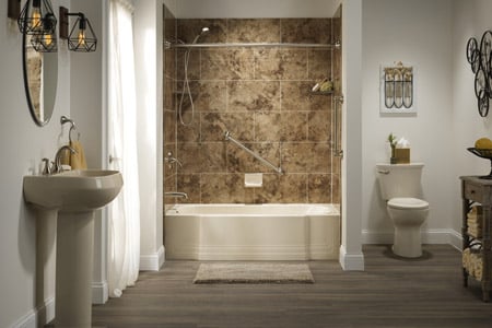 Bathroom with brown-toned tile shower and bath combination, gray wood-look flooring, pedestal sink with mirror, light fixtures, toilet, wall art, and vanity.
