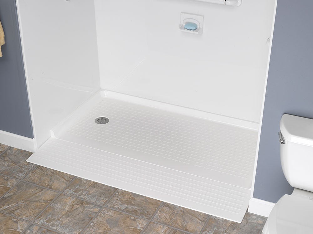 Barrier-free shower installation with textured floor and integrated soap dish, adjacent to a toilet in a bathroom.