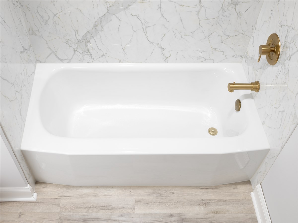 Close-up of a white bathtub with gold fixtures against a marble-patterned wall.