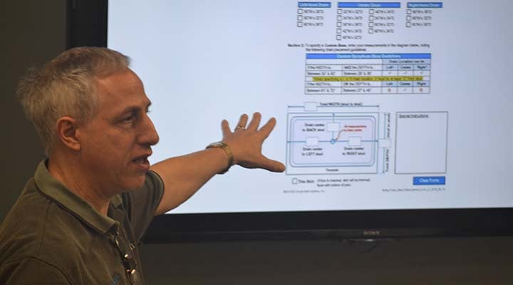Man pointing to a diagram on a presentation screen showing custom structure drain guidelines, with a table and a diagram of drain locations.